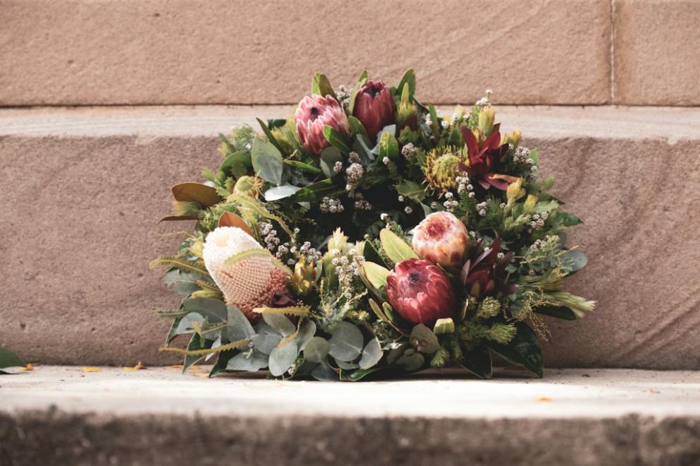 Elegant floral wreath with protea blooms and greenery resting against a stone wall, symbolizing remembrance and tribute at cemeteries Glenpool, OK.