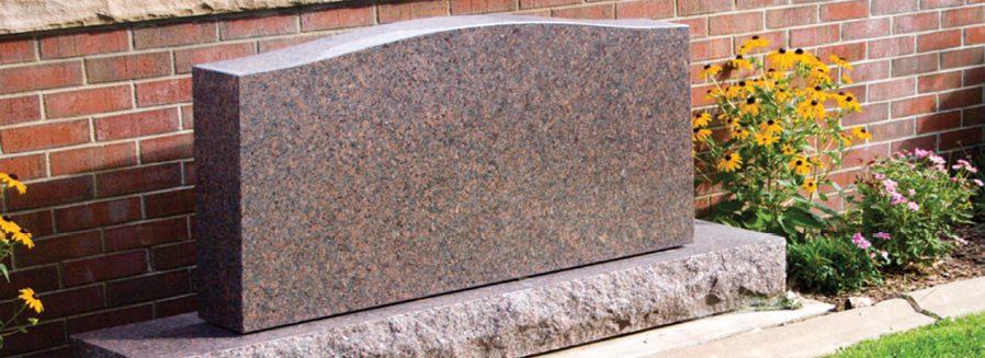 Granite memorial bench monument set against a brick wall with blooming flowers, reflecting the dignified and well-maintained cemeteries Tulsa, OK.